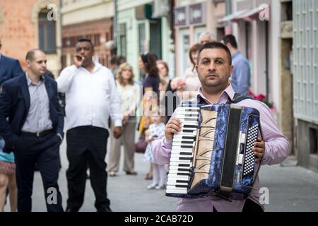 NOVI SAD, SERBIA - 12 GIUGNO 2016: Fisarmonicista con la sua fisarmonica in piedi davanti al gruppo Rom che suona musica durante un matrimonio nella capitale della t Foto Stock