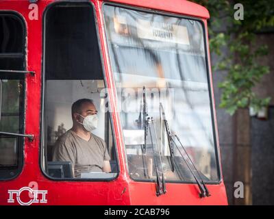 BELGRADO, SERBIA - 8 LUGLIO 2020: Viatore del tram, un uomo, che lavora nella sua cabina indossando una maschera respiratoria viso nei trasporti pubblici a Belgrado, durin Foto Stock