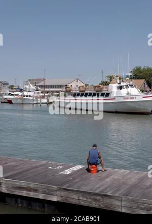 Un pescatore singolo pesca da un molo. Foto Stock