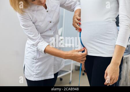 l'infermiera sta rassicurando l'altezza dello stomack della ragazza incinta. primo piano la vista laterale ritagliata foto. Foto Stock