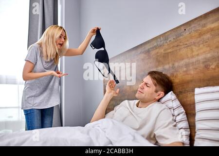 l'uomo cerca di fare scuse a sua moglie, spiega che non ha imbrogliato su di lei. donna stare in shock tenendo nero brassiere in mani, in interni Foto Stock