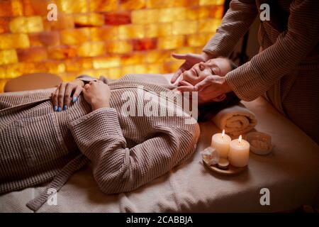 Giovane donna caucasica ottenere massaggio reacreation di testa, viso. Sdraiato sulla scrivania per i massaggi indossando accappatoio Foto Stock