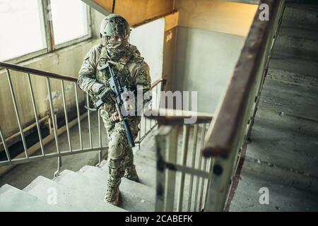 concetto di esercito. soldato con armi in atterraggio, salendo le scale, cercando nemico per sparare, proteggere. Foto Stock