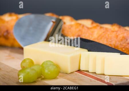 Formaggio svizzero Gruyere, affettatrice di formaggio, pane di formaggio e uva su un tagliere Foto Stock