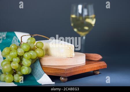 Baby Brie affumicato con uva, tovagliolo e bicchiere di vino chardonnay Foto Stock