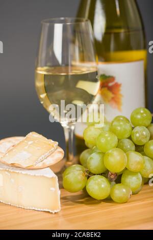 Baby Brie affumicato, uva, cracker d'acqua, bicchiere e bottiglia di vino chardonnay sul tagliere Foto Stock