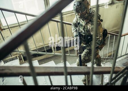 concetto di forze militari. giovane soldato va proteggere tenendo la pistola e cercando nemico in atterraggio, scale Foto Stock