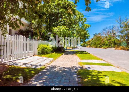 Bella vista del marciapiede con pavimentazione in pietra e cancello bianco di fronte casa in tempo di sole con cielo blu chiaro Foto Stock