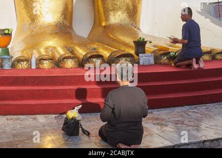 Gli adoratori si siedono e pregano ai piedi della statua dorata alta 32 m di un Buddha di Wat Indraviharn (Indrawihan) a Bangkok, Thailandia Foto Stock