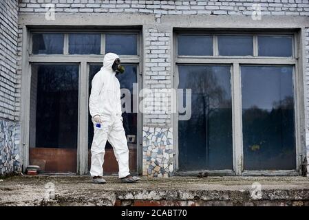 Intera lunghezza dell'ambientalista maschile in matraccio di tenuta per tuta radioattiva con liquido blu. Ricercatore che indossa tuta protettiva bianca, maschera a gas, copriscarpe. Concetto di ecologia e inquinamento ambientale. Foto Stock