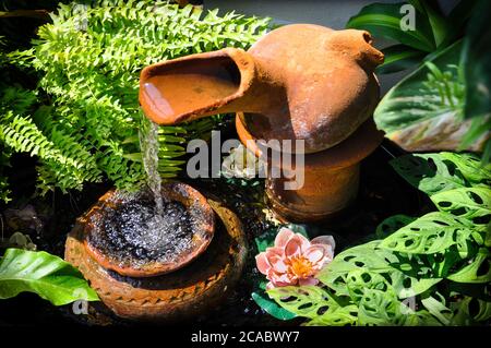 Il giardino in terracotta a cascata si presenta in un piccolo patio nel cortile, con lussureggiante vegetazione tropicale, felci e lillie d'acqua. Foto Stock