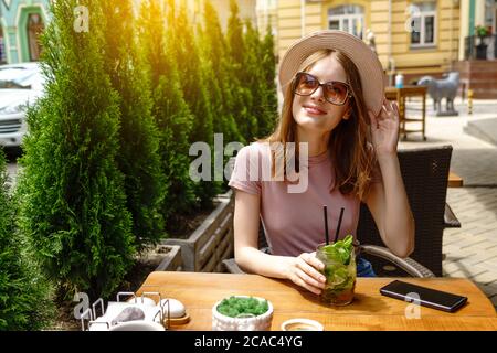 Giovane donna che beve un cocktail mojito sulla terrazza del caffè durante il caldo giorno d'estate Foto Stock