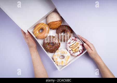 Colpo di testa di una femmina che tiene una scatola bianca di diversi tipi di gustose ciambelle Foto Stock