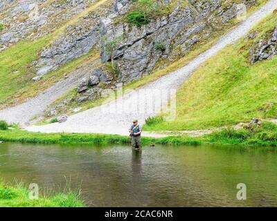 Dovedale, Derbyshire - Luglio 26 2019: Un pescatore che si trova nel fiume dove si prepara a gettare la sua linea in acqua limpida. Foto Stock
