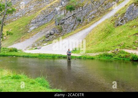 Dovedale, Derbyshire - Luglio 26 2019: Un pescatore di mosca in piedi nel fiume dove getta la sua linea fuori. Foto Stock