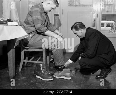 Circa, anni '40, storico, all'interno di un negozio al dettaglio Midwest americano, un giovane sitton su una sedia con il piede misurato da un venditore, per un paio di nuovi leggeri scarpe da lavoro in pelle industriale, USA. Foto Stock