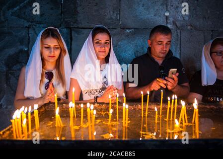 Monastero di Tatev / Armenia - 26 luglio 2019: Donne armene con testa coperta da sciarpa bianca che prega davanti alle candele nell'interno del monastero Foto Stock