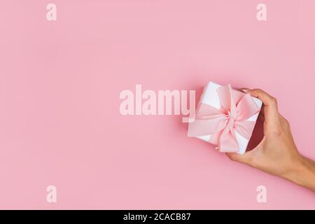 Vista dall'alto delle mani femminili che tengono la confezione presente in confezione di palmi, su sfondo rosa Foto Stock