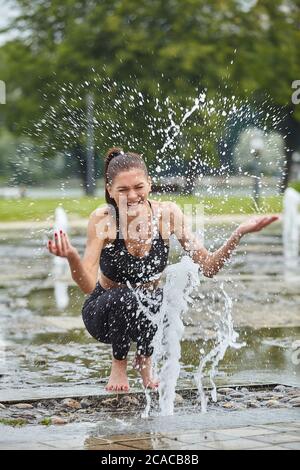 Attraente ragazza gioca felicemente con i bastoncini d'acqua fontana nel parco della città. Foto Stock