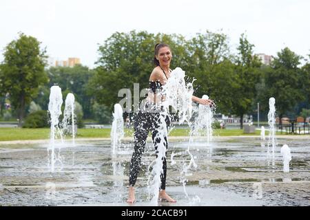 Attraente ragazza gioca felicemente con i bastoncini d'acqua fontana nel parco della città. Foto Stock