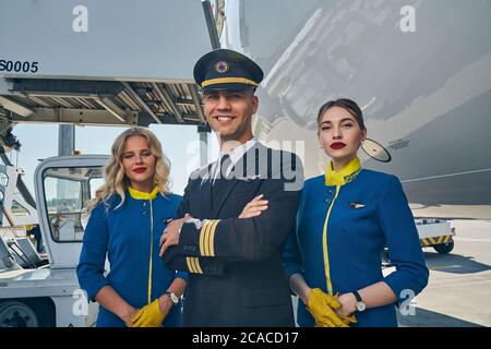 L'airman è soddisfatto con le braccia ripiegate e due stewardesses Foto Stock