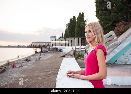 Sukhumi / Abkhazia - 2 agosto 2019: Bella giovane donna bionda guarda al mare lungo la spiaggia al tramonto Foto Stock