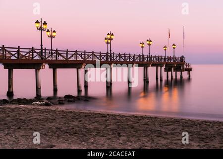 Molo illuminato in legno su una spiaggia di Marbella durante il tramonto. Esposizione lunga. Foto Stock