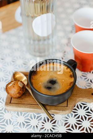 vista dall'alto caffè nero caldo in tazza di ceramica nera su vassoio di legno mettere tavolo bianco con tazze di plastica rossa e bottiglia di vetro d'acqua su tavolo bianco, copia sp Foto Stock