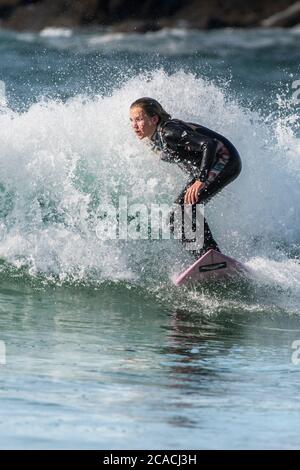 Spettacolare azione di surf come una giovane donna surfer cavalca un wave a Fistral a Newquay in Cornovaglia. Foto Stock