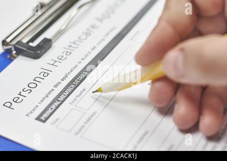 Mano di una persona che compila una domanda di assicurazione sanitaria Foto Stock
