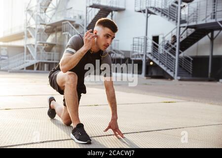 Immagine di un sportivo caucasico non rasato in auricolari che fanno esercizio mentre si lavora in aree urbane all'aperto Foto Stock