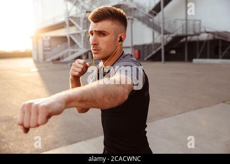 Immagine di un sportivo caucasico non rasato in auricolari che pugilato mentre si lavora in aree urbane all'aperto Foto Stock