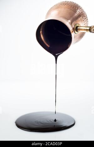 Colpo verticale di uno sciroppo di cioccolato che è versato giù da una pentola cezve su una superficie bianca Foto Stock