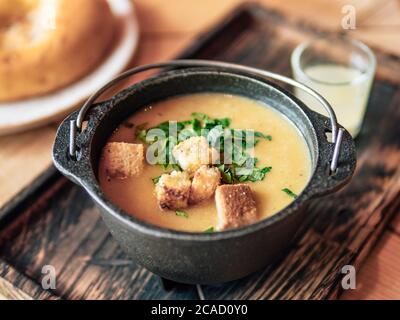 Purea zuppa con crostini e prezzemolo verde in vecchio recipiente di metallo su vecchio vassoio di legno autentico shot di zuppa di crema gialla. Foto Stock