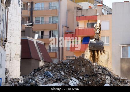 un escavatore con benna rompe un vecchio edificio residenziale. Foto Stock
