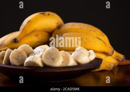 Un mazzo di banane e una banana tagliata in una ciotola su un tavolo Foto Stock