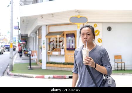 L'uomo asiatico tiene il tè del latte di ghiaccio della palla di bolla davanti al negozio sul sentiero esterno della strada. Foto Stock
