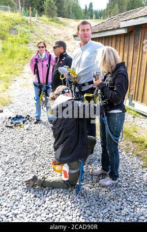 Un gruppo di turisti che sono dotati di imbracature di sicurezza da un istruttore per un'attività zip wire più in alto nelle montagne vicine a Whistler Vill Foto Stock