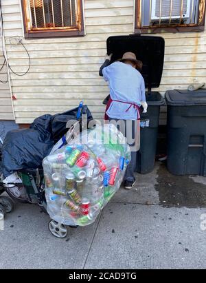 L'uomo lavora duro raccogliendo le lattine di alluminio scartate per graffiare fuori una vita lungo una strada a Brooklyn, New York. Foto Stock