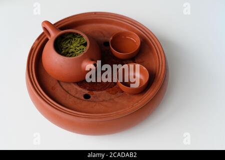 Primo piano teiera e teiera in ceramica rossa marrone con cottura a sabbia su sfondo bianco. Le foglie di tè fresco galleggiano sull'acqua del tè. Tradizionale cultura del tè cinese Foto Stock