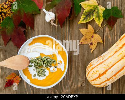 Ciotola di zuppa di zucca invernale guarnita con semi di zucca e crema pesante su un rustico tavolo di legno. Foto Stock