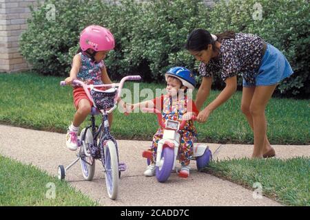 Austin Texas USA: Giovani ragazze ispaniche che imparano ad andare in bicicletta in sicurezza mentre sono supervisionate dalla babysitter ispanica. ©Bob Daemmrich Foto Stock