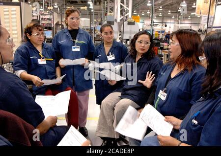 Matamoros, Messico, aprile 2006: I dipendenti femminili che indossano camici da laboratorio e occhiali di sicurezza tengono una piccola riunione per discutere della produzione giornaliera presso il reparto di produzione di Delphi Delco Electronics de Mexico. L'impianto di maquiladora, appena oltre il confine degli Stati Uniti da Brownsville, Texas, produce radio e altre parti per le auto della General Motors. Delphi ha circa 11.000 lavoratori messicani in sette fabbriche vicino a Matamoros. ©Bob Daemmrich Foto Stock