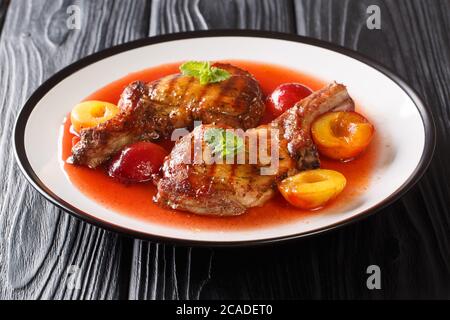 Porzione di carne di maiale alla griglia trita con prugne e salsa di frutta da vicino in un piatto sul tavolo. Orizzontale Foto Stock