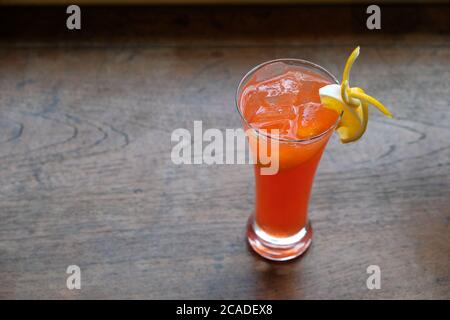 primo piano un bicchiere di cocktail arancione con fetta di frutta su tavolo in legno a motivi geometrici. sfondo sfocato Foto Stock