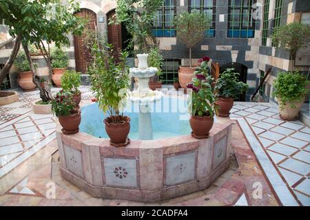 Una fontana ad acqua decagonale e piante in vaso in un tradizionale cortile siriano all'aperto in una casa nel vecchio quartiere di Damasco, Siria. Foto Stock