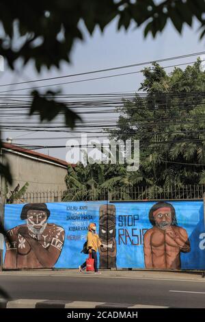 Depok, Indonesia. 05 agosto 2020. Una donna passa accanto a un murale raffigurante una persona indigena papuana dalla pelle scura come campagne murali contro il razzismo al pubblico.l'Indonesia ha 1,331 gruppi etnici con cultura, caratteri e colori della pelle diversi. Con gente di colore scuro dalle tribù che abitano le province di Papua e Papua occidentale. Attualmente, spesso ricevono un trattamento diseguale e uno stigma da parti della società indonesiana. Credit: SOPA Images Limited/Alamy Live News Foto Stock