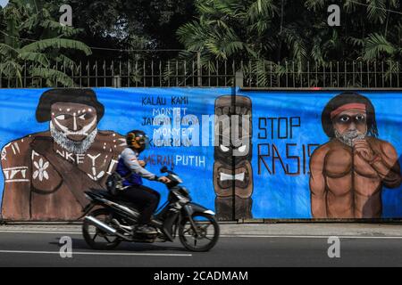 Depok, Indonesia. 05 agosto 2020. Un motociclista passa davanti a un murale raffigurante una persona indigena papuana dalla pelle scura come campagna murale contro il razzismo al pubblico. L'Indonesia ha 1,331 gruppi etnici con cultura, personaggi e colori della pelle diversi. Con gente di colore scuro dalle tribù che abitano le province di Papua e Papua occidentale. Attualmente, spesso ricevono un trattamento diseguale e uno stigma da parti della società indonesiana. Credit: SOPA Images Limited/Alamy Live News Foto Stock