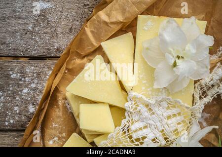 Pezzi di burro di cacao con pizzo e fiori bianchi. Cioccolato bianco su carta di colore marrone. Foto Stock