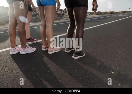 Atlete multietniche irriconoscibili in piedi su strada asfaltata durante la sessione di corsa in serata in periferia Foto Stock